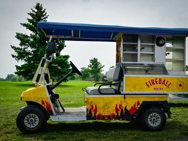 Voiturette de service habillée aux couleurs de Fireball Whisky sur un terrain de golf