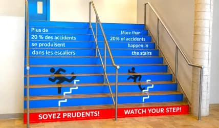 Graphiques de sécurité bilingues appliqués sur les contremarches d’un escalier